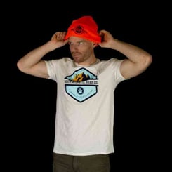 A man wearing a white T-shirt with a mountain logo and text adjusts his bright orange NASC Beanie against a black background.