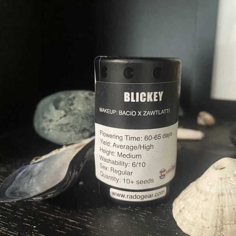 A black cylindrical container labeled "Blickey (R) [ZAWTLATTI DROP]" with details about its contents, including flowering time, yield, height, washability, sex, and quantity. Various stones and shells are artfully placed around it.