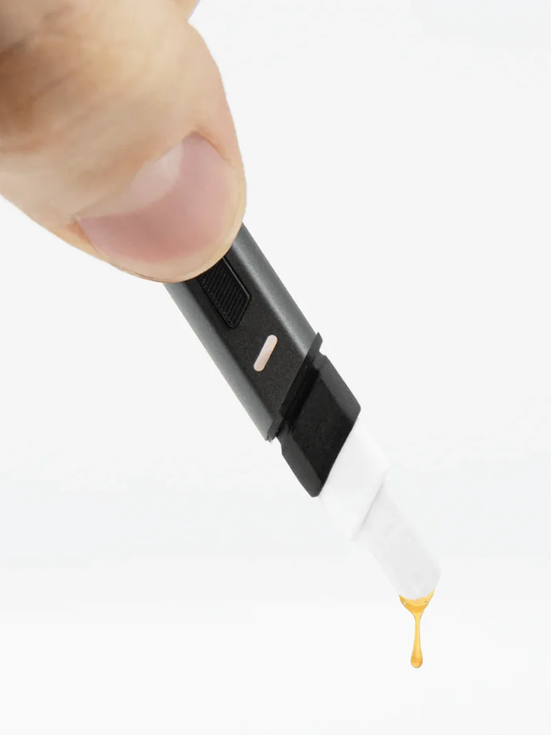 A hand holding a black and white Hot Knife with a brown liquid droplet at the tip, reminiscent of the precision of a hot knife slicing through butter.